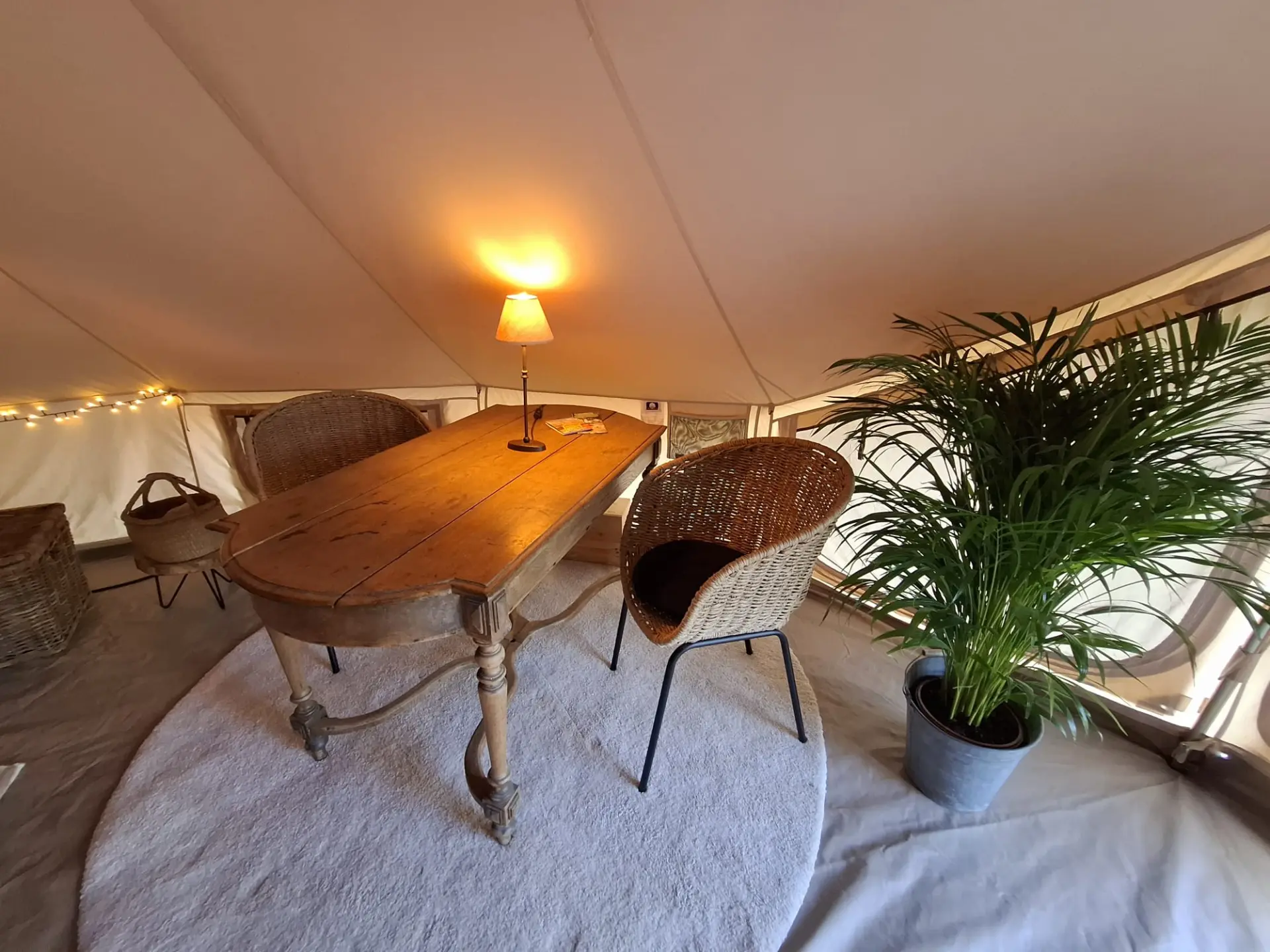 Houten eettafel met rieten stoelen en schemerlamp in de glampingtent