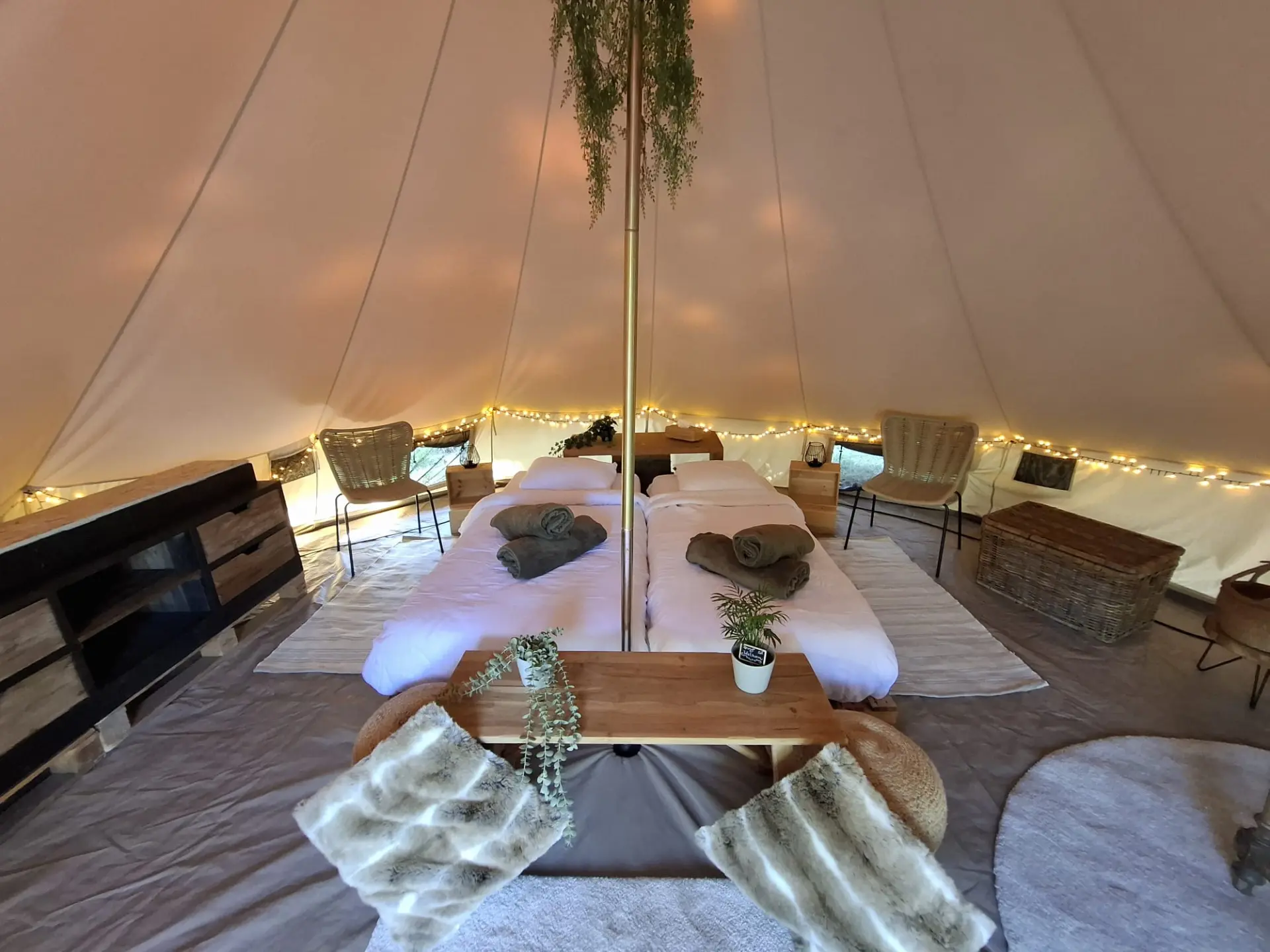 Interieur van de glampingtent met twee bedden, lichtjes en een zithoek